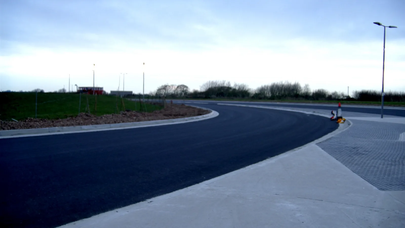 A newly surfaced highway junction with new kerbing and temporary traffic management, before road markings are applied.