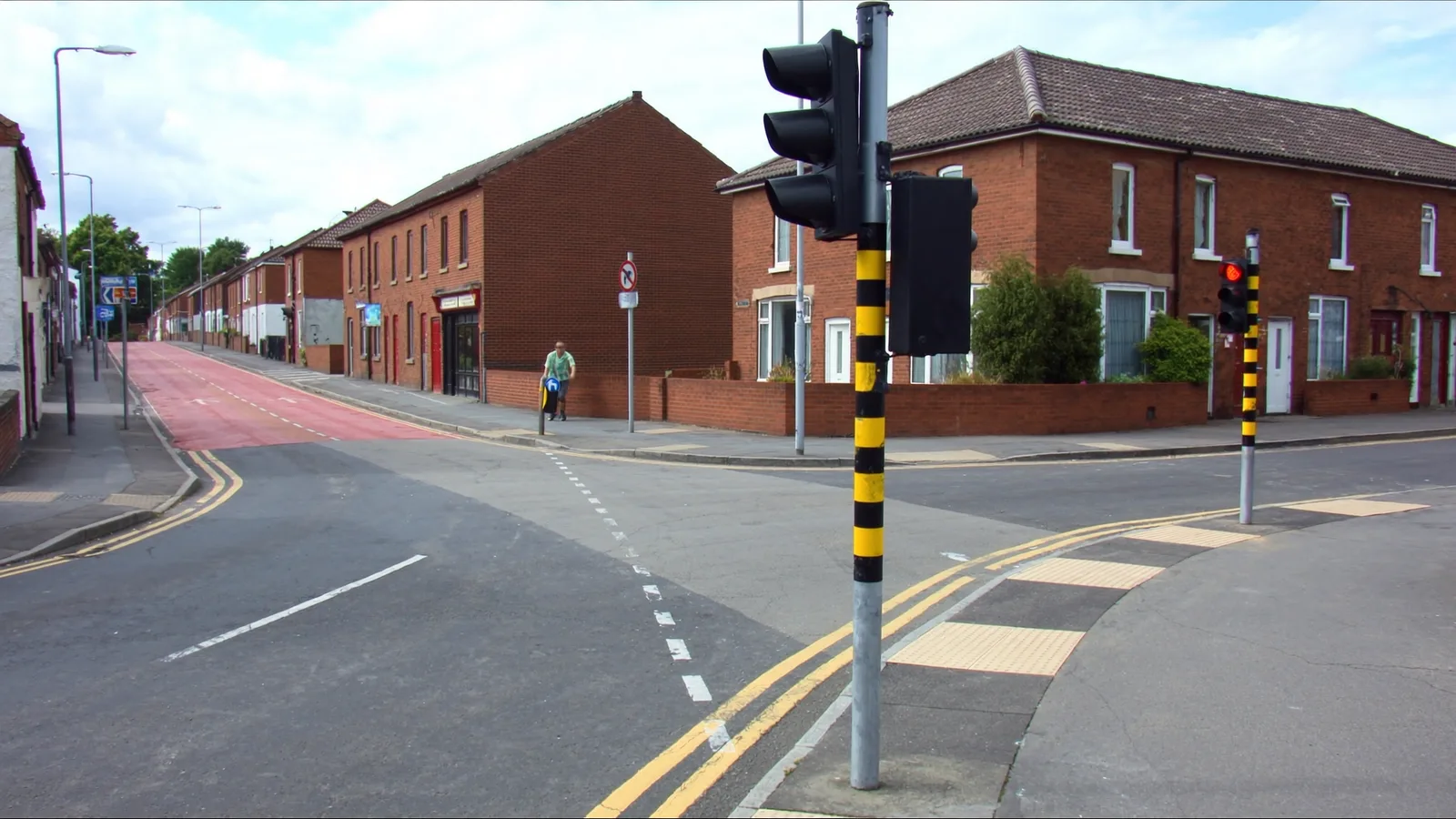 Newly installed traffic signal heads on galvanised poles at a British urban junction, with tactile paving and new chamber covers in the footway.